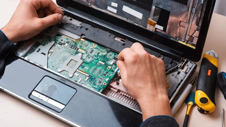 Kéz egy laptop belsejében, processzor cseréjéhez szükséges alkatrészekkel.