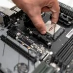Egy kéz éppen egy processzort helyez el egy alaplapra, amely modern számítógéphez készült.