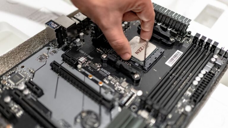 Egy processzor éppen egy alaplapra kerül, miközben a háttérben alkatrészek láthatók.