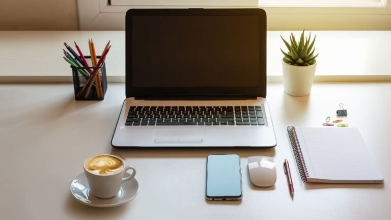 Egy íróasztal, amin laptop, kávé, telefon és írószerek találhatók.