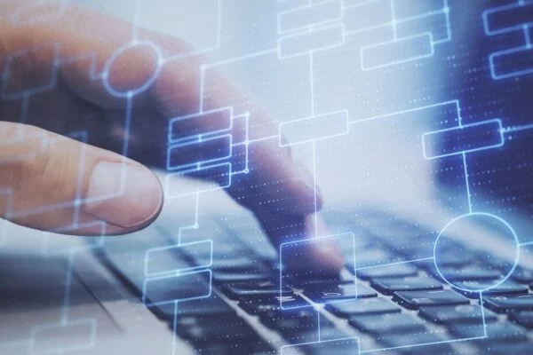 Egy kéz gépel egy laptop billentyűzetén, digitális diagramokkal körülvéve.