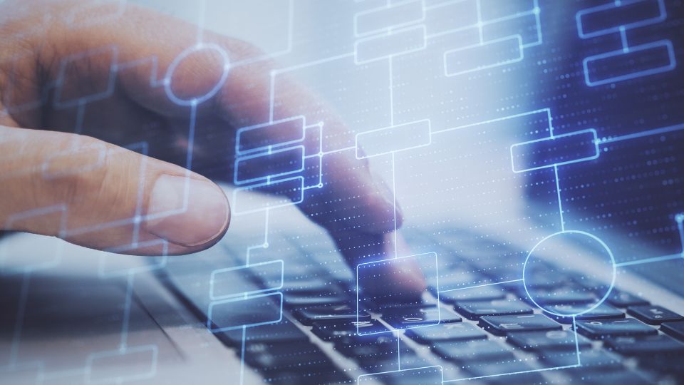Egy kéz gépel egy laptop billentyűzetén, digitális diagramokkal körülvéve.