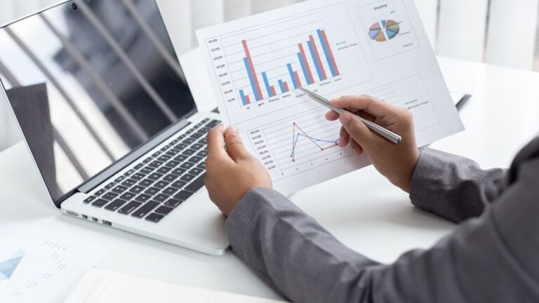 Egy üzletember grafikonokat és adatokat néz egy laptop mellett.
